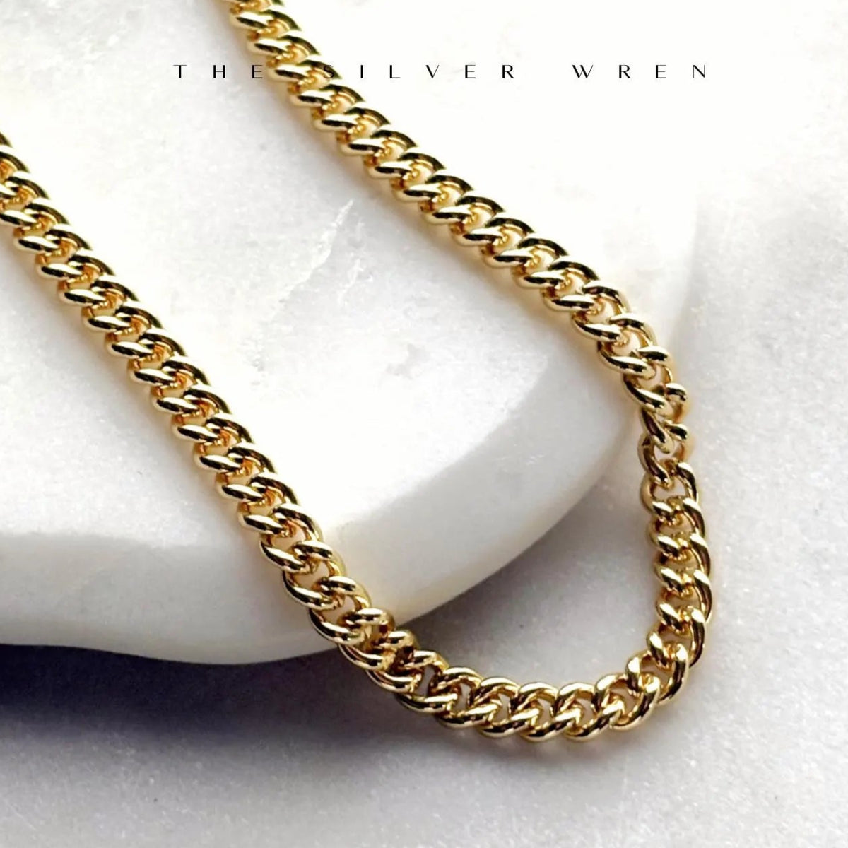 A gold chain necklace laid out on a white surface, showcasing its chunky and link design.