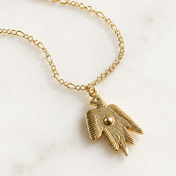 A gold-toned layered chain necklace with a textured bird pendant, displayed on a light marble background with branding text for 'The Silver Wren' and feature icons on the left.