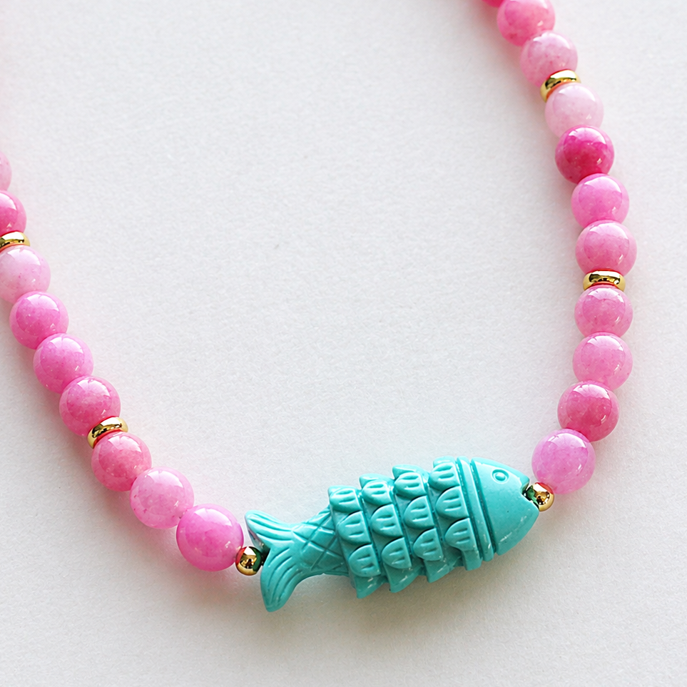 Necklace with pink beads and a turquoise fish charm on a white background