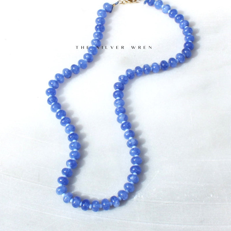 A handcrafted beaded necklace with blue cornflower candy color beads and 14kt gold plated accents, displayed against a white background.