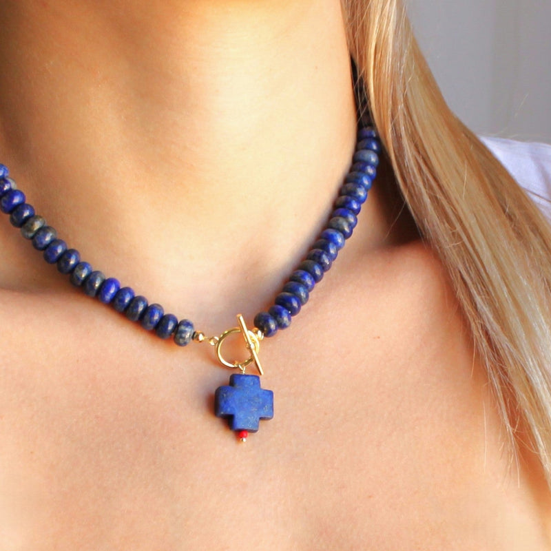 Blue beaded necklace with a unique pendant on a person wearing a white top.