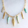 Necklace with gold and turquoise fish pendants on a light gray background
