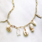 Gold necklace with shell and fish charms on a light background
