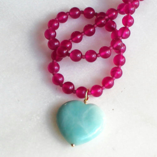 Necklace with pink beads and a turquoise heart pendant on a white background