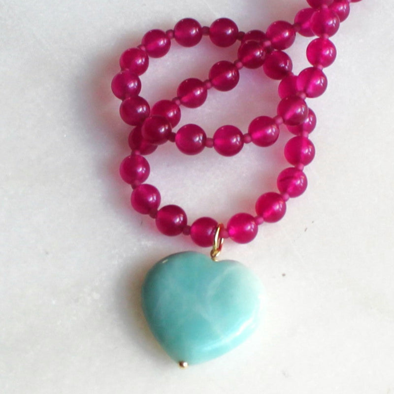 Necklace with pink beads and a turquoise heart pendant on a white background