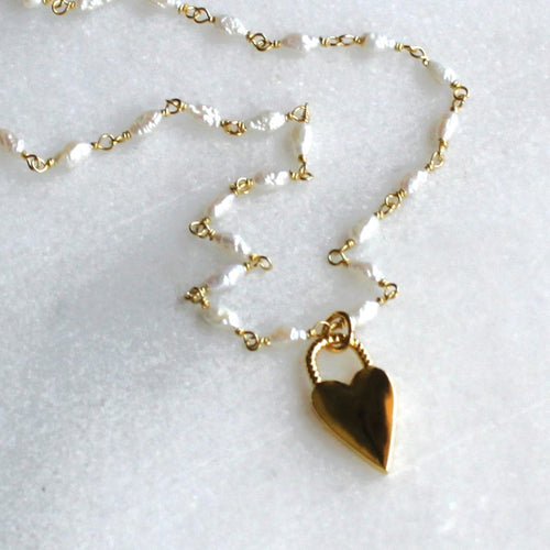 Gold necklace with a heart pendant on a light gray background