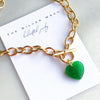 Gold chain necklace with a green heart pendant on a branded card