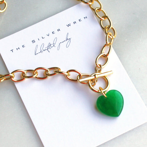 Gold chain necklace with a green heart pendant on a branded card