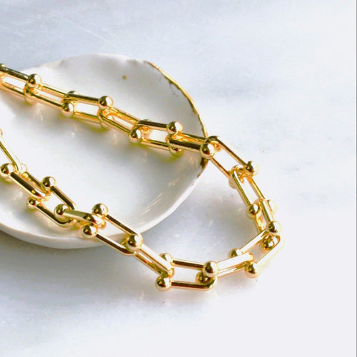 Gold chain necklace on a white dish with a white background