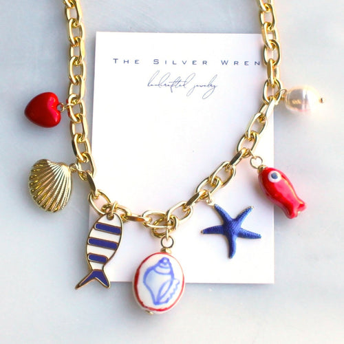 Gold necklace with colorful charms on a white card, featuring 'The Silver Wren' brand.
