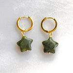 Gold hoop earrings with green star-shaped charms on a white background