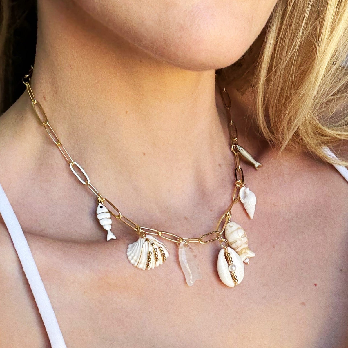 Necklace with shell pendants worn by a person in a white top.