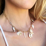 Necklace with shell pendants worn by a person in a white top.