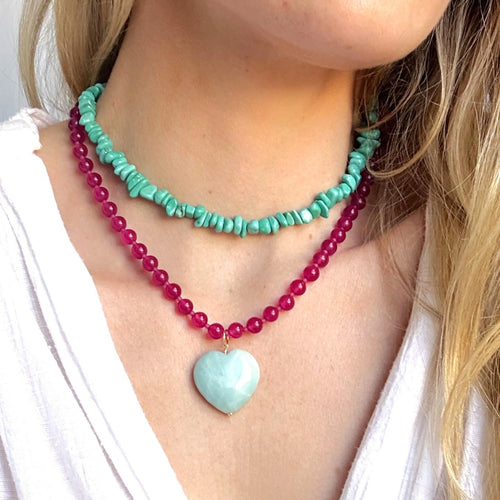 Close-up of a woman wearing two necklaces with a heart pendant on a plain background
