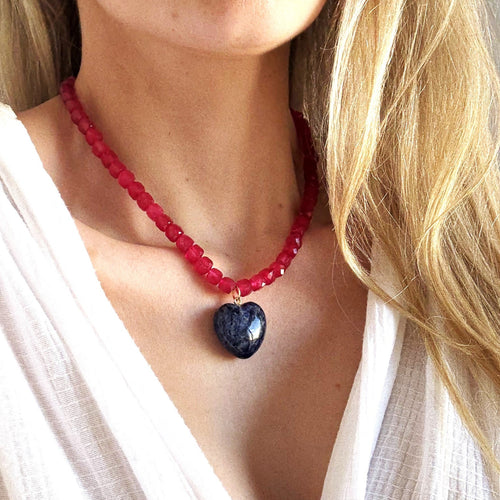 Necklace with red beads and a dark blue heart pendant worn by a person in a white top.