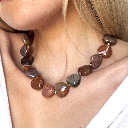 Necklace with brown and gray stones worn by a person in a white outfit.