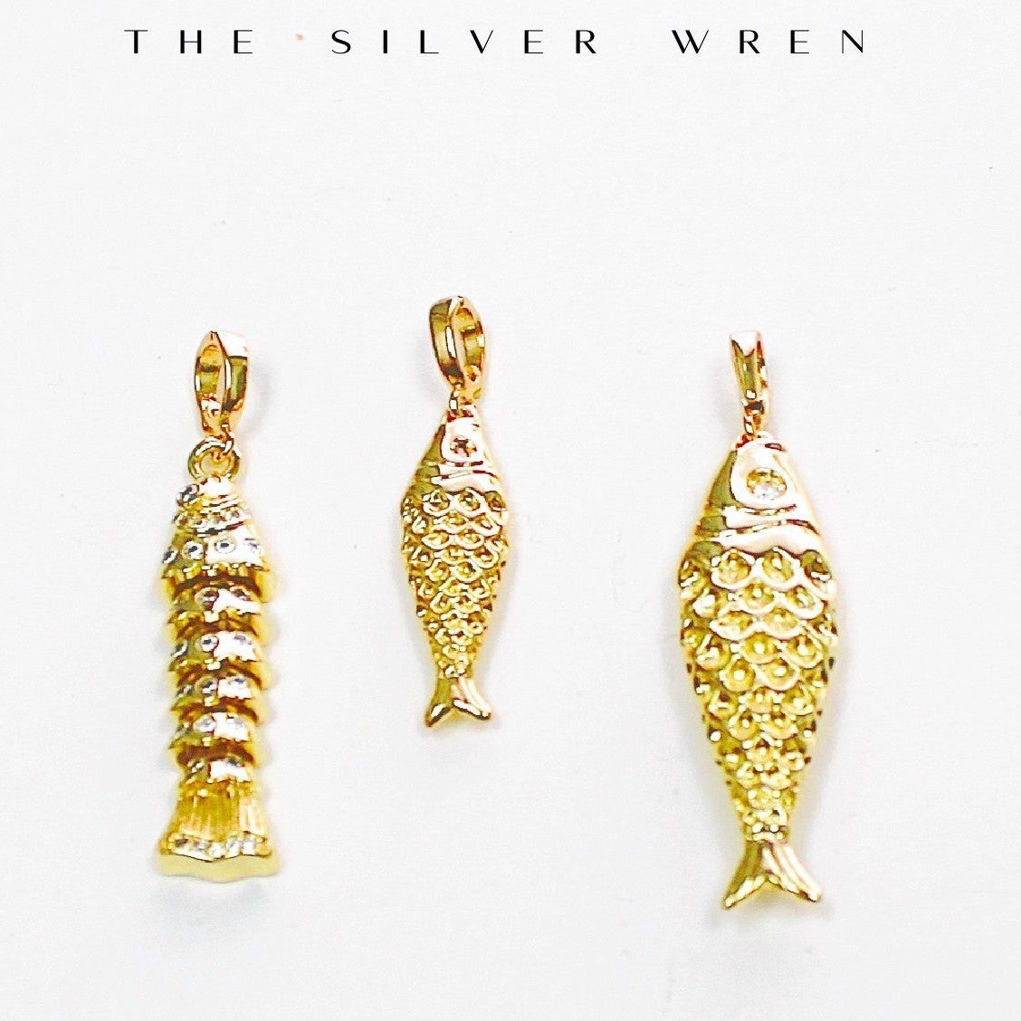 Three gold fish-shaped pendants on a white background with 'The Silver Wren' branding.