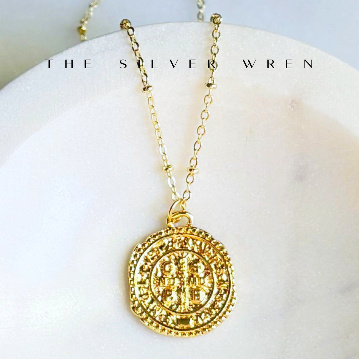 Gold necklace with a circular pendant on a white surface, branded 'The Silver Wren'.