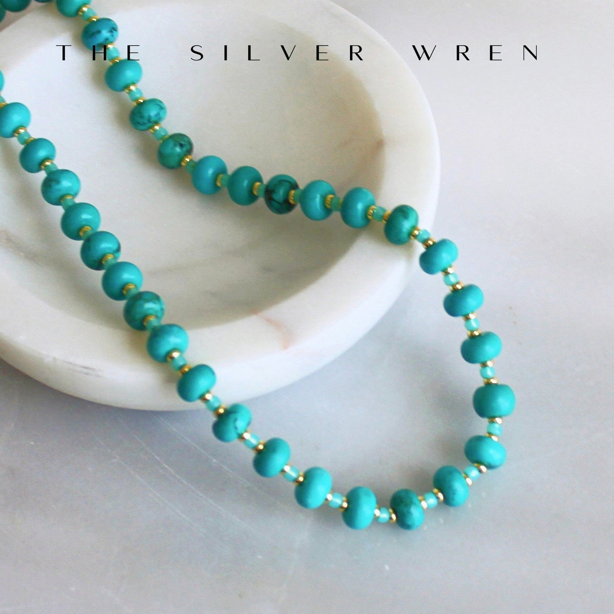 Turquoise beaded necklace on a white marble surface with 'The Silver Wren' branding.