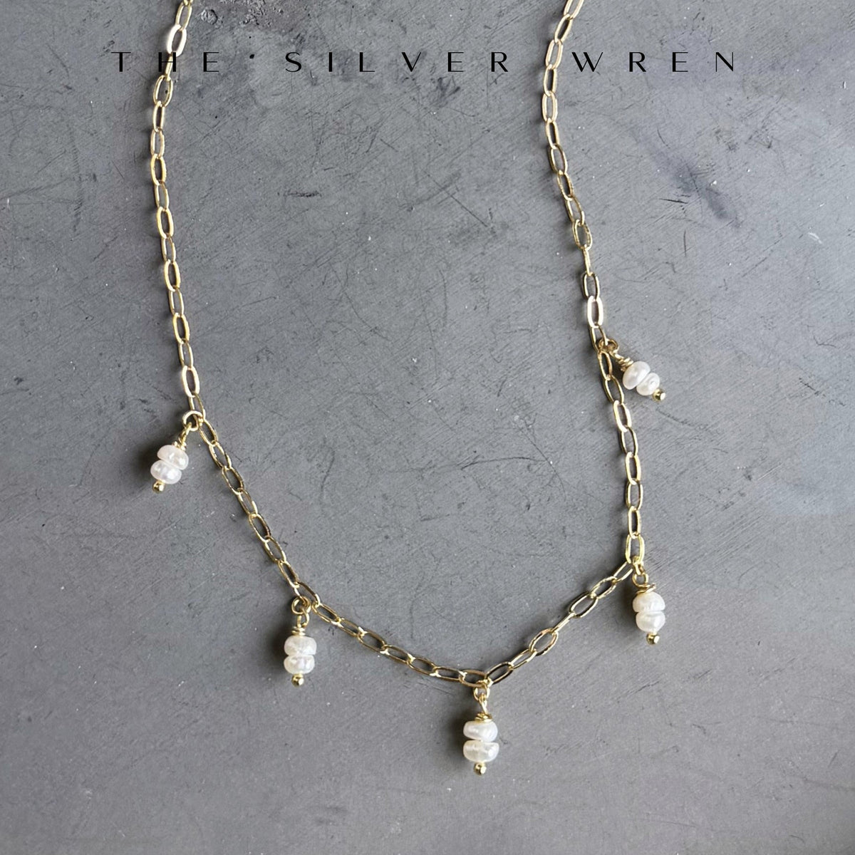 Gold chain necklace with pearl drops on a gray background, branded 'The Silver Wren'.