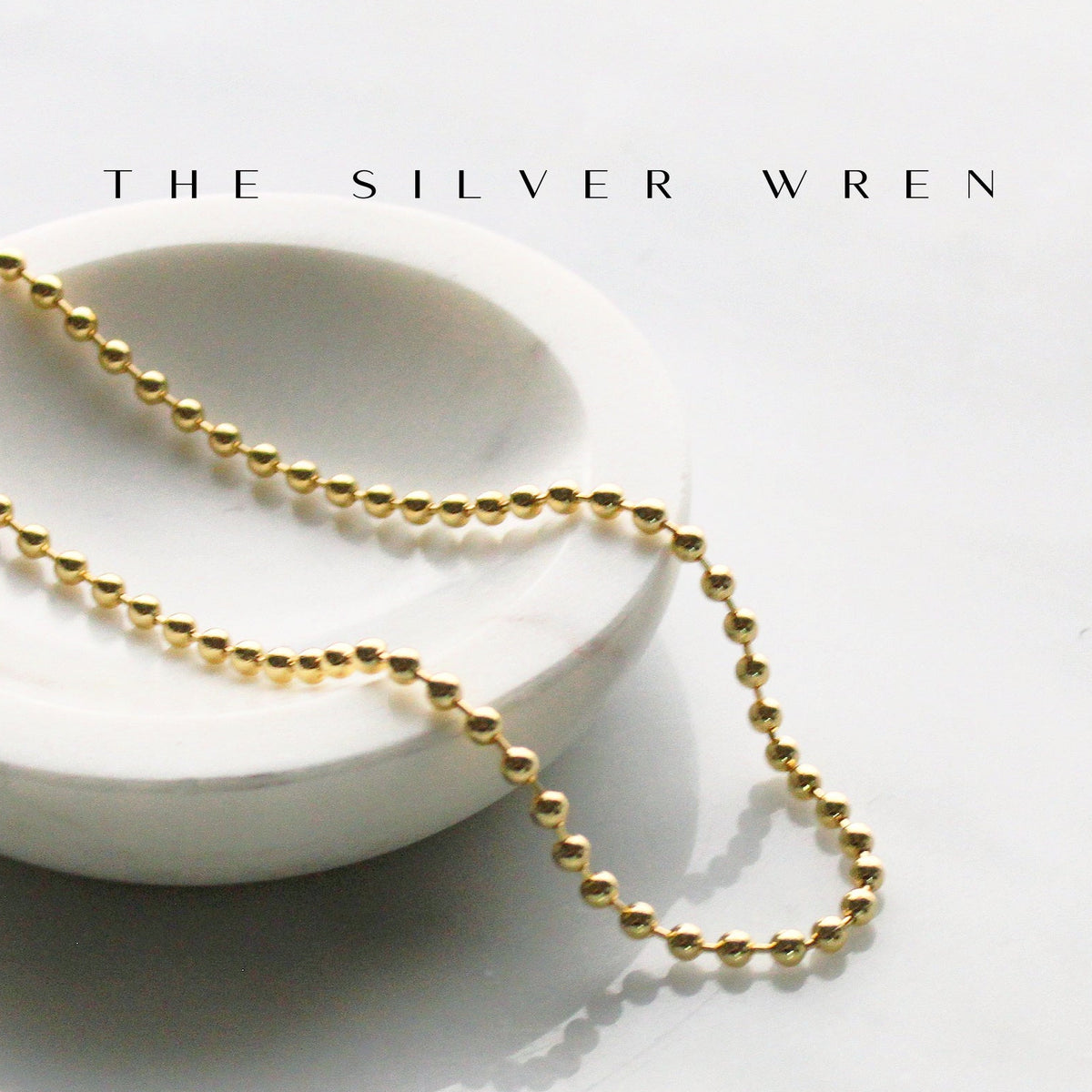 Gold chain necklace on a white dish with 'The Silver Wren' branding.