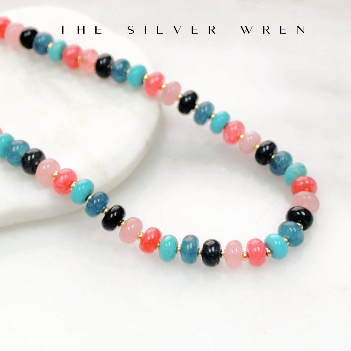 Colorful beaded necklace on a white surface with 'The Silver Wren' branding.