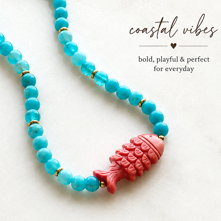A turquoise blue beaded necklace with a pink fish charm and gold spacer beads, displayed on a light marble background with promotional text.