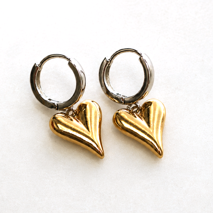 A pair of silver hoop earrings with layered gold heart charms, displayed on a textured off-white background with brand and feature text.