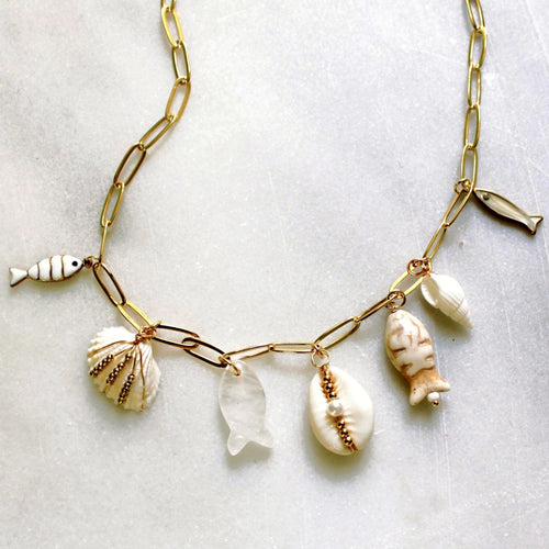 Gold necklace with shell and fish charms on a light background