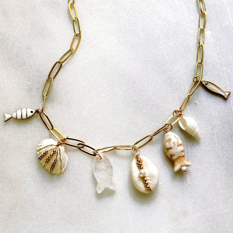 Gold necklace with shell and fish charms on a light background