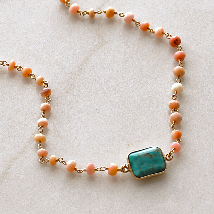 A beaded necklace with peach, orange, and white gemstone beads connected by gold-toned chains, featuring a rectangular turquoise-blue stone pendant. The necklace is displayed on a light marble surface next to text badges that read 'THE SILVER WREN', 'GENUINE GEMSTONES', 'HANDMADE', and 'TIMELESS DESIGN'.